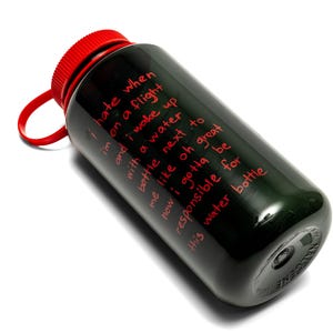 May include: Black water bottle with a red cap and a red loop. The bottle has red text that reads: "I hate when I'm on a flight and I wake up with a water bottle next to me like oh great now I gotta be responsible for this water bottle."