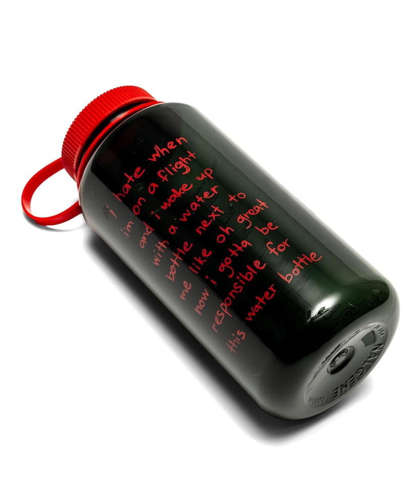 May include: Black water bottle with a red cap and a red loop. The bottle has red text that reads: "I hate when I'm on a flight and I wake up with a water bottle next to me like oh great now I gotta be responsible for this water bottle."