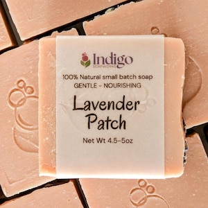 Peut inclure: Une collection de savons carrés rose clair, chacun arborant un motif floral estampé. Un savon est entouré d'une étiquette en papier portant l'inscription Indigo Soapworks, 100% Natural small batch soap, GENTLE - NOURISHING, Lavender Patch.