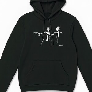 May include: Black hooded sweatshirt with a front pocket and a drawstring. The sweatshirt features a black and white graphic of two men in suits pointing guns. The graphic is centered on the chest.