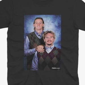 May include: Black t-shirt featuring a portrait of two people wearing argyle vests over button-down shirts. The image has a blue background and the text "Futbol Classics" is visible.