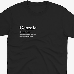 Puede incluir: Camiseta negra con la definici&oacute;n de "Geordie" impresa en blanco. La definici&oacute;n incluye la pronunciaci&oacute;n, la parte de la oraci&oacute;n y una breve descripci&oacute;n: "Speaks in vowels, lives for matchday, fears nowt."