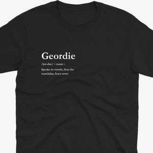 May include: Black t-shirt with the definition of "Geordie" printed in white. The definition includes the pronunciation, part of speech, and a brief description: "Speaks in vowels, lives for matchday, fears nowt."