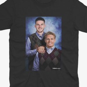 May include: Black t-shirt with a photo of two men wearing sweaters. The men are smiling and standing next to each other. The background is a blue and white gradient.