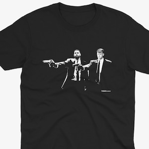 Op de afbeelding: Zwart-wit T-shirt met een grafische print van twee mannen in pak die wapens vasthouden, met de tekst "Pulp Fiction" onderaan.