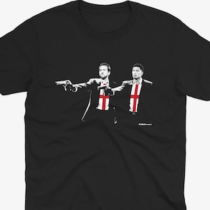 Könnte beinhalten: Schwarzes T-Shirt mit einer Grafik von zwei Figuren in Anzügen, die jeweils eine Waffe halten. Die Figuren haben die englische Flagge auf der Brust. Das Design ist in Weiß und Rot gehalten.