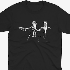 May include: Black t-shirt featuring a white graphic of two men in suits pointing guns. The image is a stylized illustration, with the figures in a dynamic pose. The design is a pop culture reference.