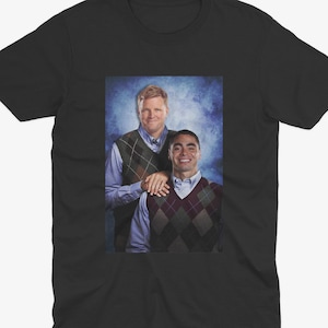 May include: A black t-shirt with a photo of two men wearing sweaters. The man on the left is wearing a green and brown sweater and the man on the right is wearing a red and white patterned sweater.