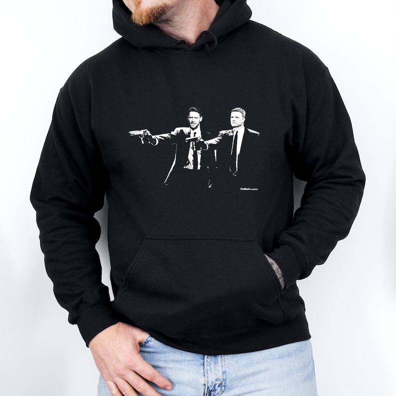 May include: Black hoodie with a white graphic of two men in suits, each holding a gun. The design is a stylized illustration. The hoodie has a front pocket and a hood.