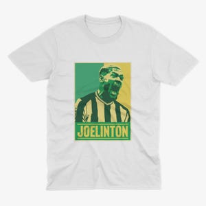 May include: White t-shirt with a green, yellow, and black graphic of a soccer player with the text "JOELINGTON" in yellow.