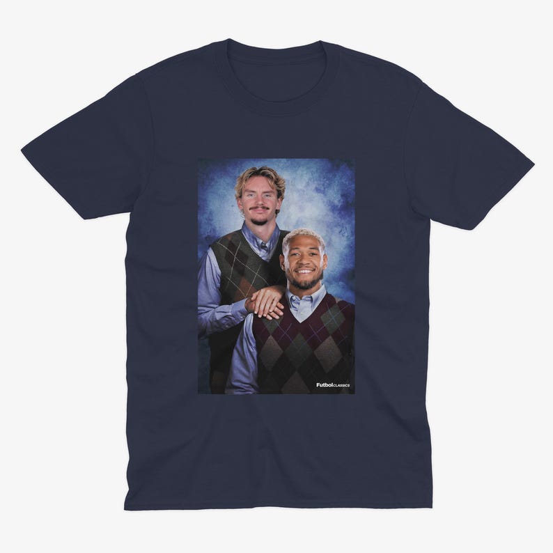 May include: Navy blue t-shirt featuring a portrait of two people wearing argyle vests over collared shirts. The image has a vintage aesthetic with a blue background. The text "Futbol Classics" is visible in the bottom right corner.