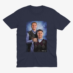 May include: A navy blue t-shirt featuring a photograph of two men wearing sweaters. The men are standing in front of a blue and white background. The text "Football Classics" is printed at the bottom of the image.