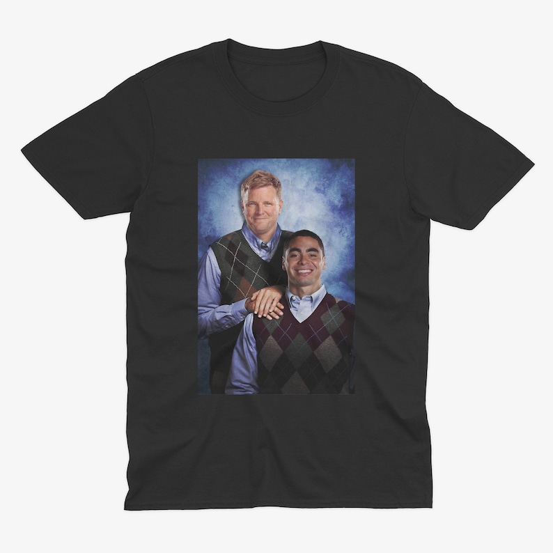 Peut inclure: Un t-shirt noir avec une photo de deux hommes portant des pulls. L'homme &agrave; gauche porte un pull vert et marron et l'homme &agrave; droite porte un pull &agrave; motifs rouge et blanc.