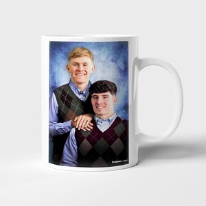 May include: White ceramic mug with a portrait of two people wearing argyle vests and collared shirts. The mug has a handle on the right and the text "FutbolClassics" on the bottom right.