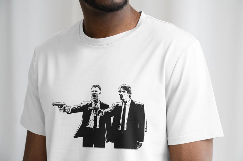 May include: White t-shirt featuring a black and white graphic of two men in suits pointing guns. The image is a stylized illustration, with one man yelling. The shirt is made of a soft material.