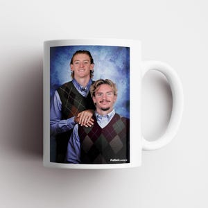 May include: White ceramic mug featuring a humorous image of two men in argyle vests and collared shirts against a blue backdrop. The mug has a white handle and the text "FutbolClassics" is printed on the bottom.