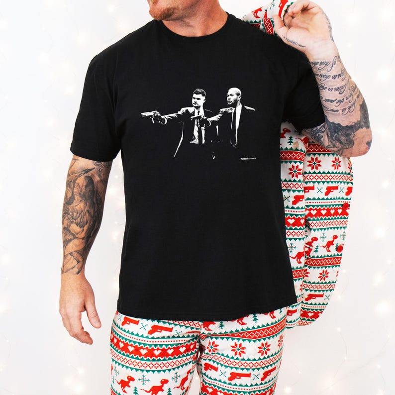 May include: Black t-shirt featuring a stylized black and white graphic of two men pointing guns. The image is a movie reference. The person in the image is wearing Christmas-themed pajamas.