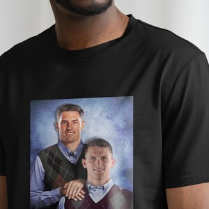 Puede incluir: Una camiseta negra con una imagen impresa de dos hombres que llevan jers&eacute;is estampados. Los hombres est&aacute;n de pie frente a un fondo azul y blanco.
