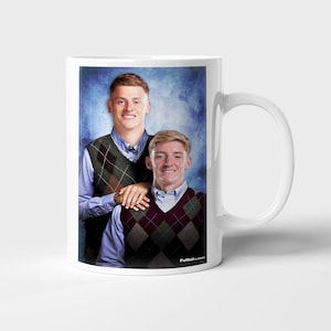 May include: White ceramic mug featuring a portrait of two people wearing argyle vests over button-down shirts. The background is a textured blue. The mug has a white handle and the text "FutbolClassics" is visible on the bottom right.