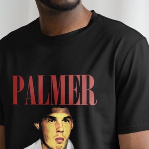 May include: Black t-shirt with a red "PALMER" graphic and a portrait of a man in the center.