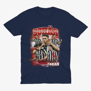 May include: A navy blue t-shirt featuring a retro-style graphic of a football player, Fabian Sch&auml;r, wearing a black and white jersey with the number 5. The graphic is surrounded by red lightning bolts and the text "Fabian" and "Sch&auml;r" in red.