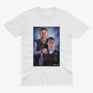 Puede incluir: Una camiseta blanca con una foto de dos hombres con su&eacute;teres. Los hombres est&aacute;n de pie uno al lado del otro y sonriendo. El fondo es un degradado azul y blanco.