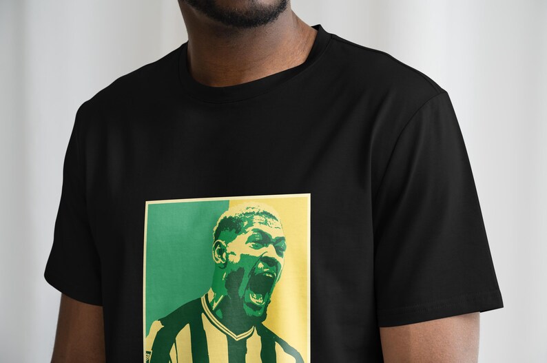 May include: Black t-shirt with a green and yellow graphic print of a man's face. The man is wearing a striped jersey.
