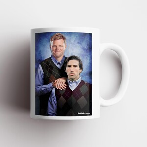 May include: White ceramic mug featuring a portrait of two men in argyle vests and collared shirts against a blue background. The mug has a white handle and the text "FutbolClassics" is printed on the bottom.