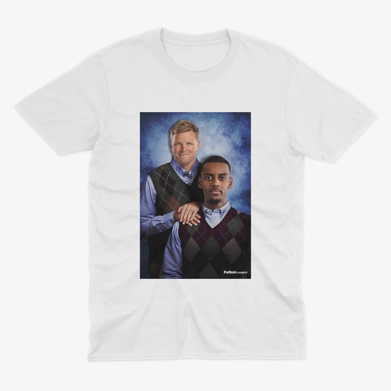 May include: A white t-shirt with a photo of two men wearing sweaters. The man on the left is wearing a green and brown patterned sweater and the man on the right is wearing a burgundy and white patterned sweater. The text "Fullback Classics" is at the bottom of the image.