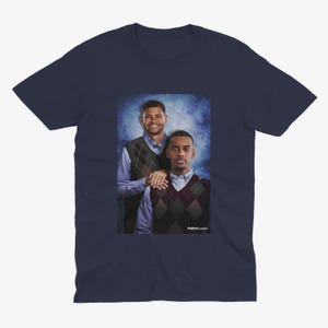 May include: A navy blue t-shirt featuring a photograph of two men wearing sweaters. The men are standing in front of a blue and white background. The text "Fullback Classics" is printed at the bottom of the photograph.