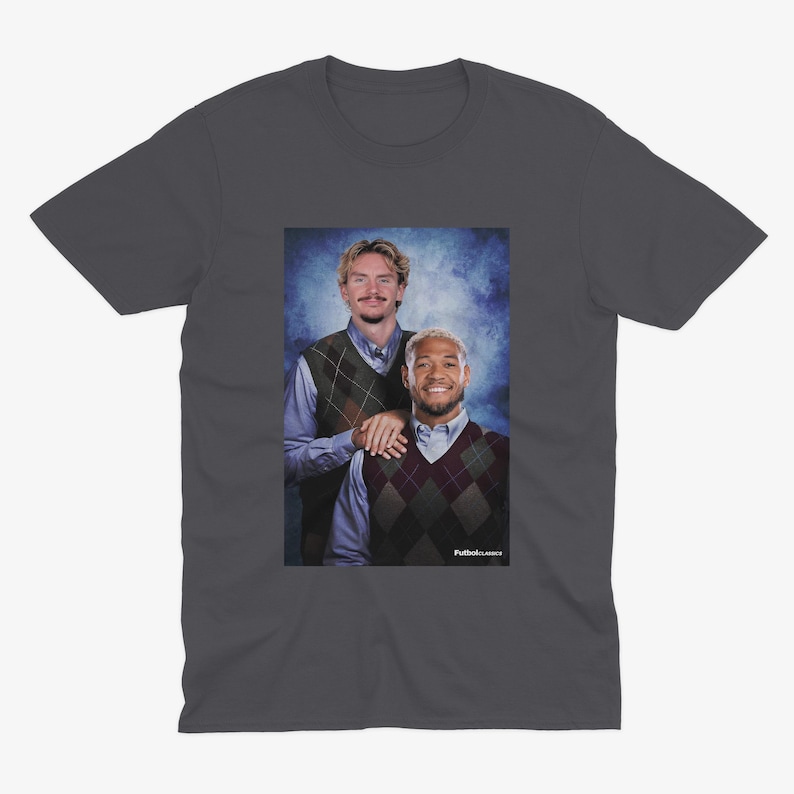 May include: Dark gray t-shirt featuring a portrait of two men in argyle vests and collared shirts. The image has a vintage aesthetic. The text "Futbol Classics" is visible in the bottom right corner.
