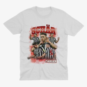 May include: White t-shirt featuring a red and white graphic of a football player with the text "SCH&Auml;R FABIAN" on the front.