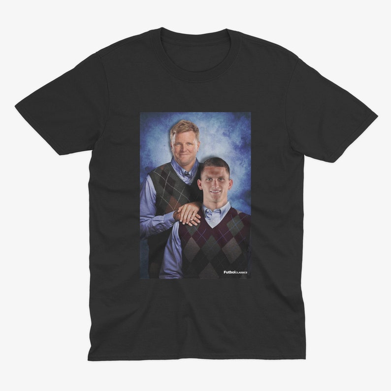 Op de afbeelding: Een zwart T-shirt met een foto van twee mannen die truien dragen. De mannen staan ​​naast elkaar en glimlachen. De achtergrond is een blauwe en witte gradi&euml;nt.