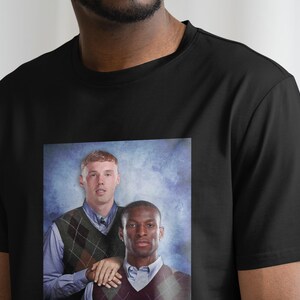 May include: A black t-shirt with a printed image of two men in a school photo. The men are wearing sweaters with a diamond pattern. The background is a blue and white gradient.