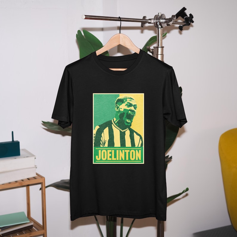 May include: Black t-shirt with a retro-style graphic of a soccer player with the text "JOELINGTON" in yellow.