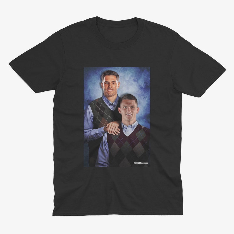 Puede incluir: Una camiseta negra con una foto de dos hombres con su&eacute;teres. Los hombres est&aacute;n de pie uno al lado del otro y sonriendo. El fondo es un degradado azul y blanco.