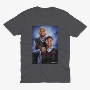 May include: A dark gray t-shirt with a photo of two men wearing sweaters. The man on the left is wearing a green and white patterned sweater and the man on the right is wearing a burgundy and white patterned sweater. The text "Fullback Classics" is at the bottom of the image.