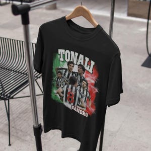 Puede incluir: Camiseta negra con un gr&aacute;fico de estilo vintage de jugadores de f&uacute;tbol. El gr&aacute;fico presenta el texto "Tonali Sandro" y una bandera italiana.