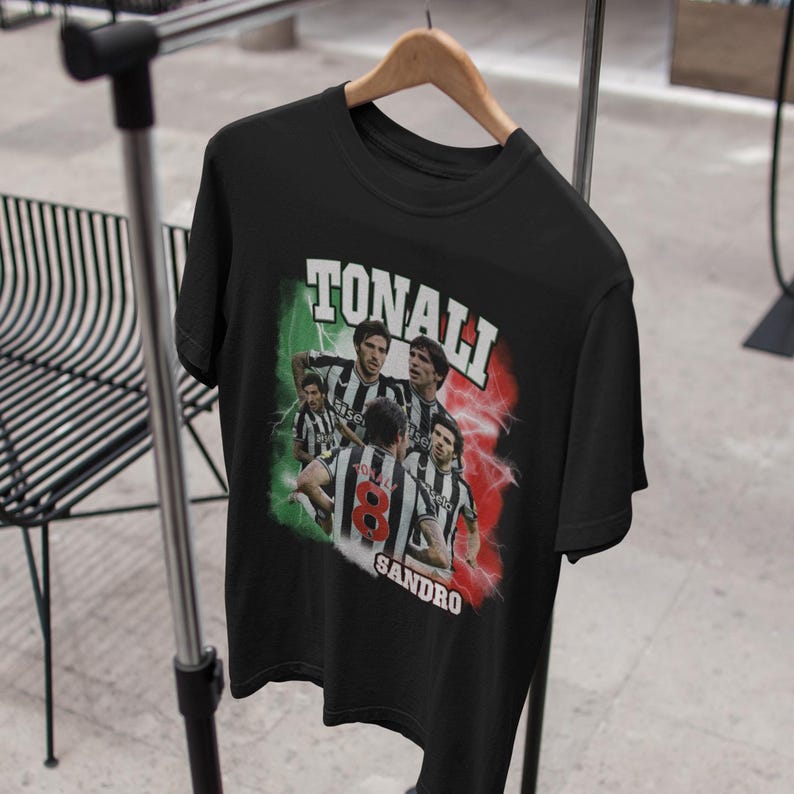 Puede incluir: Camiseta negra con un gr&aacute;fico de estilo vintage de jugadores de f&uacute;tbol. El gr&aacute;fico presenta el texto "Tonali Sandro" y una bandera italiana.