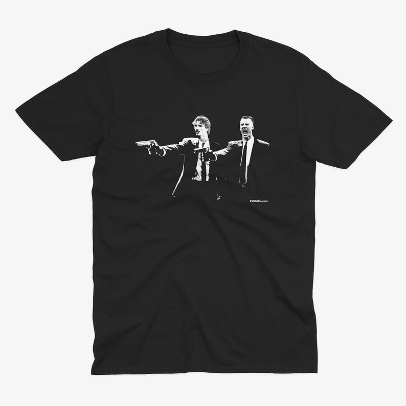 May include: Black t-shirt featuring a white graphic of two men in suits pointing guns. The image is a stylized illustration, with the figures in a dynamic pose. The design is a pop culture reference.