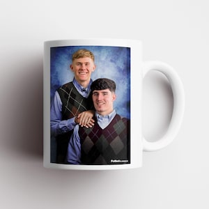May include: White ceramic mug with a portrait of two people in argyle vests and blue shirts. The mug has a white handle and the text "FutbolClassics" is visible on the side.