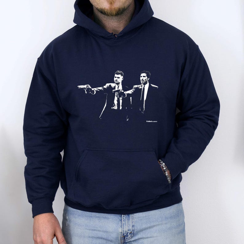 May include: Navy blue hoodie featuring a black and white graphic of two figures in suits pointing guns. The graphic is a stylized illustration. The hoodie has a front pocket and a drawstring hood.