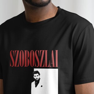 K&ouml;nnte beinhalten: Schwarzes T-Shirt mit einem roten Grafikdruck des Namens "SZOBOSZLAI" und einem Schwarzwei&szlig;foto eines Mannes im wei&szlig;en Anzug.