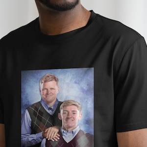 May include: A black t-shirt with a printed image of two men in a blue and white patterned sweater vest. The men are smiling and standing next to each other.