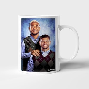 May include: White ceramic mug featuring a portrait of two smiling people wearing argyle vests over button-down shirts. The background is a textured blue. The mug has a white handle and the text "FutbolClassics" is visible.
