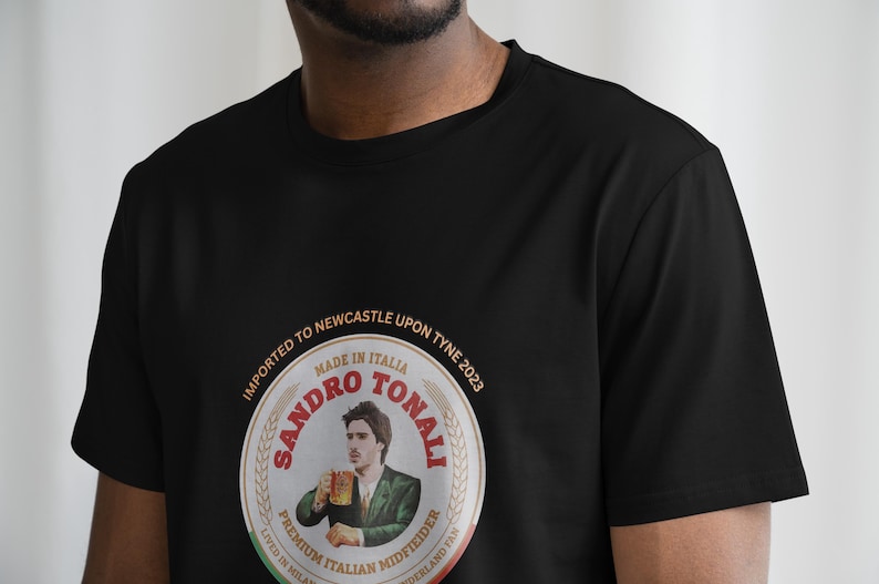 Pu&ograve; includere: Maglietta nera con una grafica circolare di un viso maschile con il testo "SANDRO TONALI" in font rosso e oro. La grafica include anche il testo "IMPORTED TO NEWCASTLE UPON TYNE 2023" e "MADE IN ITALIA".
