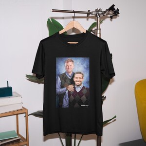 May include: Black t-shirt with a photo of two men wearing sweaters. The men are smiling and standing next to each other. The photo is set against a blue background.