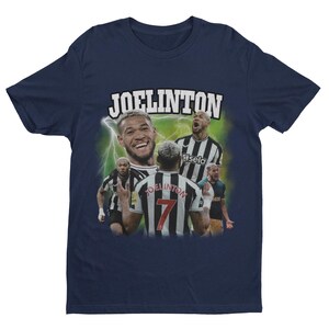 Pode incluir: Uma camiseta azul marinho com um gr&aacute;fico de estilo retr&ocirc; do jogador de futebol Joelinton. O gr&aacute;fico mostra Joelinton vestindo uma camisa listrada preta e branca com o n&uacute;mero 7 na frente. O texto "JOELINGTON" est&aacute; impresso em letras brancas acima do gr&aacute;fico.