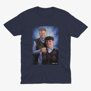 May include: A navy blue t-shirt with a photo of two men wearing sweaters. The men are standing in front of a blue and white background. The text "Puttin' on Classics" is printed on the bottom of the photo.