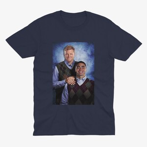 Peut inclure: Un t-shirt bleu marine avec une photo de deux hommes portant des pulls. L'homme &agrave; gauche porte un pull &agrave; motifs vert et marron et l'homme &agrave; droite porte un pull &agrave; motifs marron et blanc.